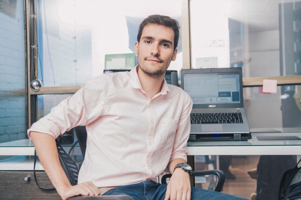 Confident young man in shirt working in modern office with laptop and desk accessories.